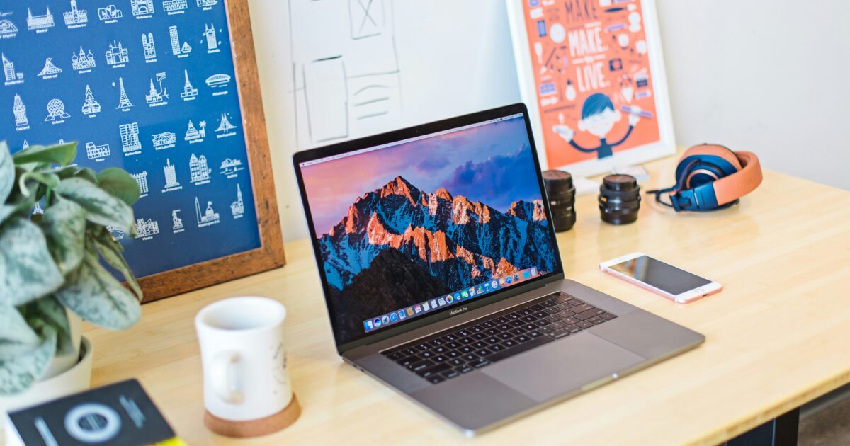 デスク上に置かれたノートパソコンと観葉植物ヘッドホンカメラレンズスマートフォンなどのガジェット類