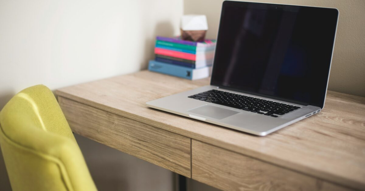 木製デスクとグリーンのチェアの上にノートパソコンと積み重ねられた本が置かれている様子