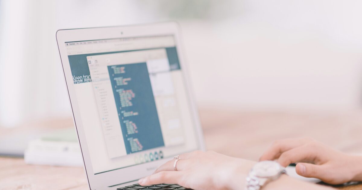 プログラムコードが表示されたノートパソコンを操作している女性の手元