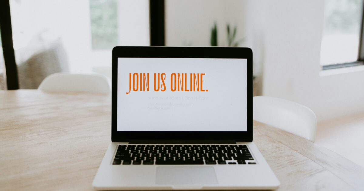 木製テーブルに置かれたノートパソコンの画面にJOIN US ONLINEの文字が表示されている様子