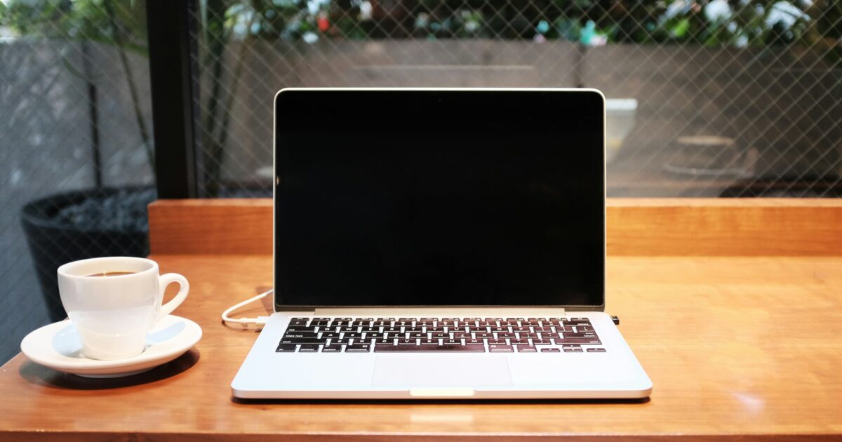 カフェの窓際カウンターに置かれたノートパソコンと白いカップのコーヒー