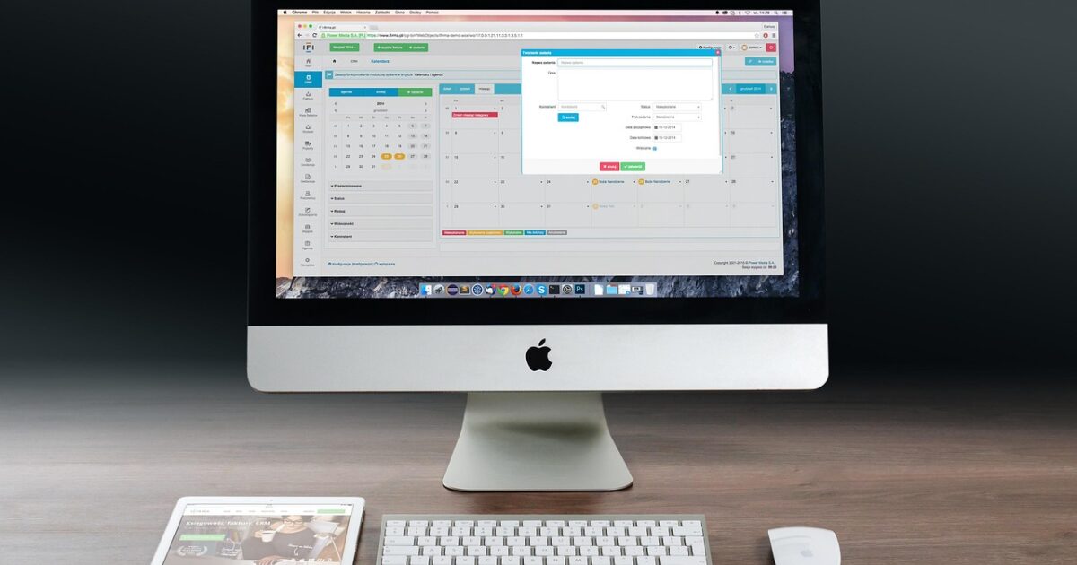 デスク上のiMacにカレンダー管理ツールが表示されタブレットとキーボードマウスが並んでいる様子