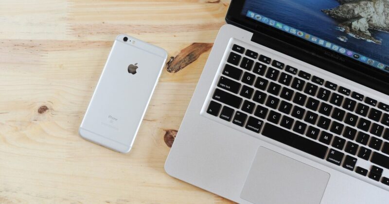 木製デスクの上に置かれたMacBook ProとシルバーのiPhoneのクローズアップ