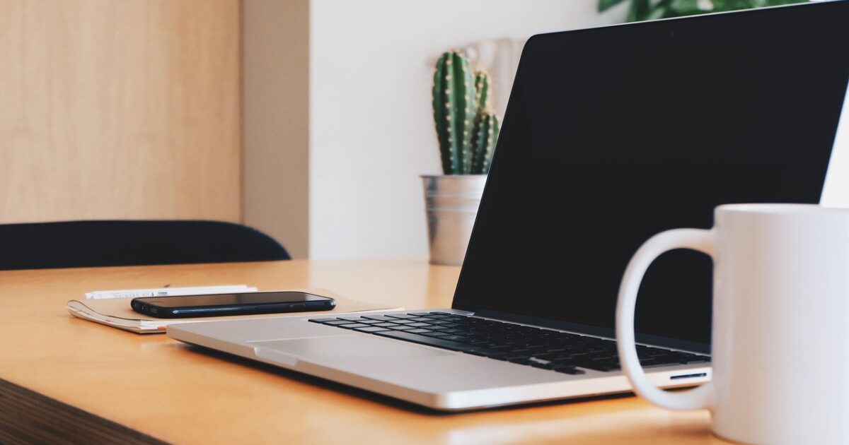 カップとスマートフォンが置かれた木製デスクにノートパソコンが設置されたワークスペース