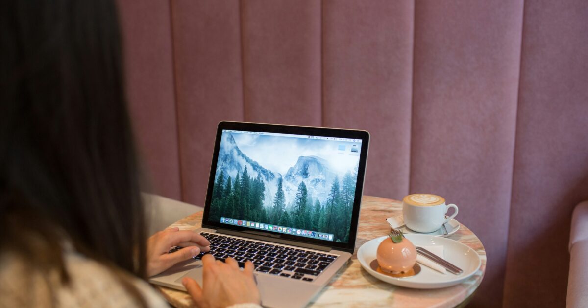 カフェのテーブルでノートパソコンを操作しながらカフェラテとスイーツが置かれている様子