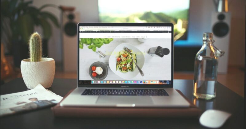 ノートパソコンに料理の写真付きウェブサイトが表示されているホームオフィスの様子